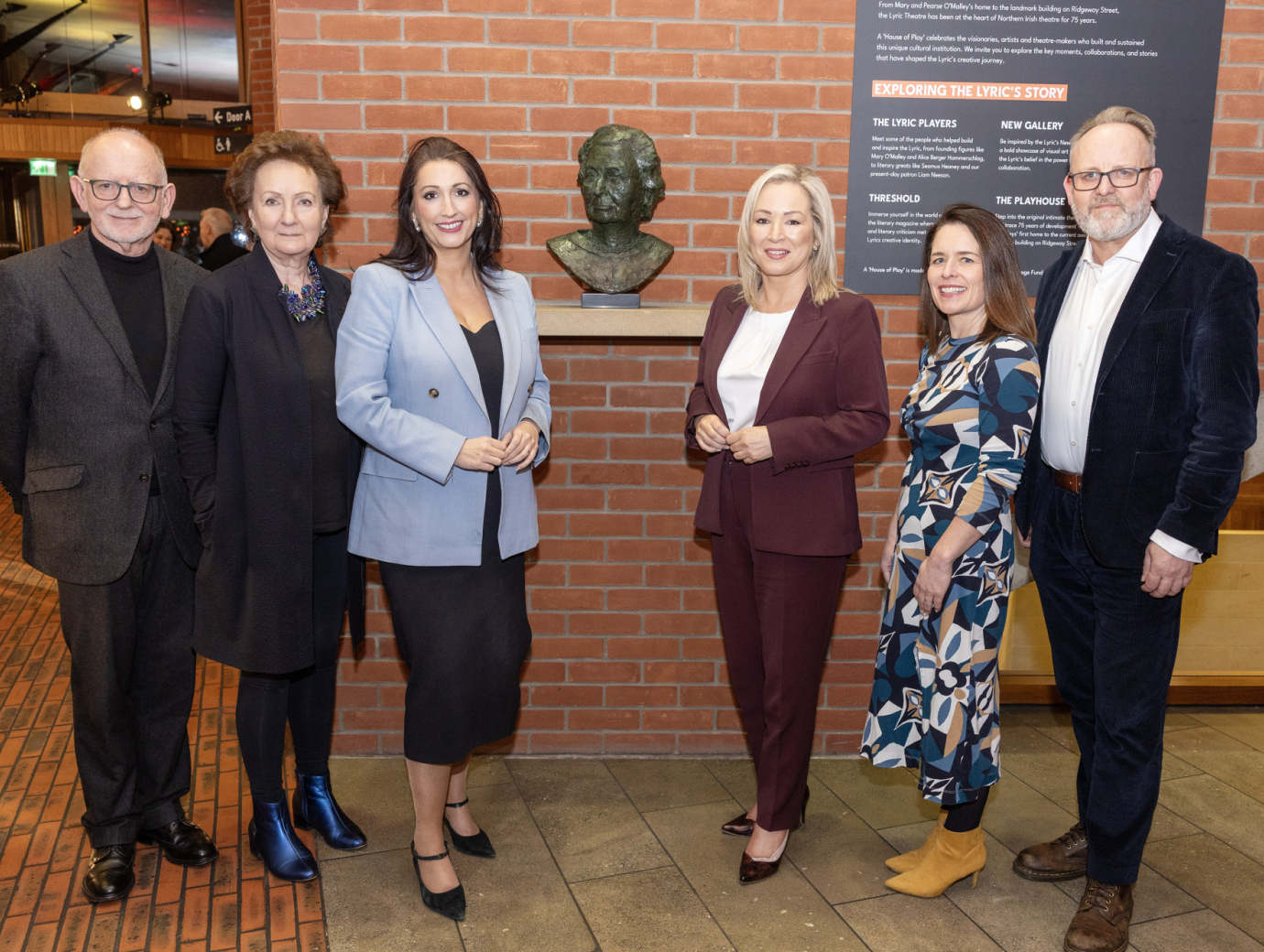 six people standing in a row in front of a statue, all looking at the camera and smiling.