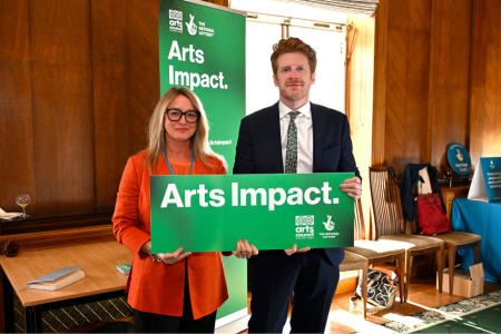 a man and a woman standing in front of a green Arts Impact banner
