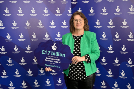 A woman standing in front of a blue screen holding a sign about national lottery funding