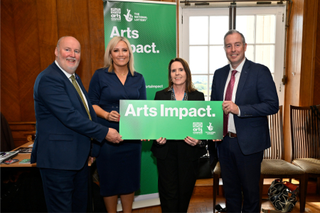 2 men and 2 women standing in front of a green banner saying Arts Impact.