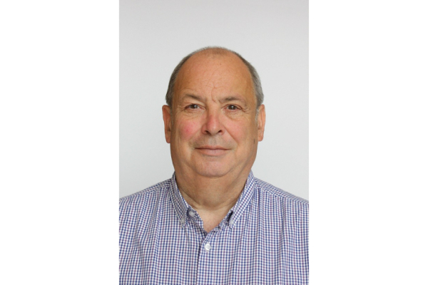Ray Hall's bio photograph. He stands against a pale grey background and wears a blue checked shirt.