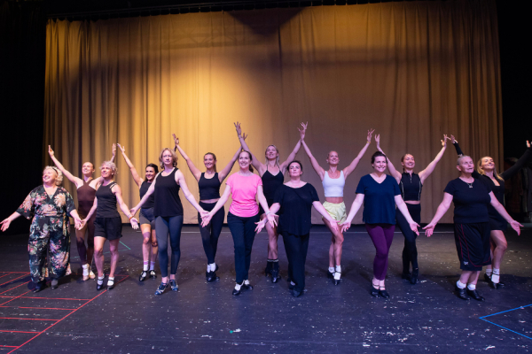A group of females on stage with their hands in the air.