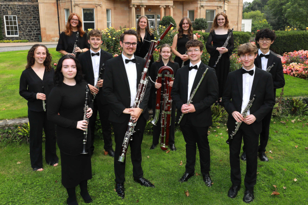 A group of woodwind musicians in black tie formal wear pose as a group with their instruments.