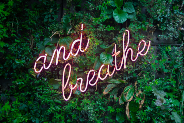 A pink neon sign with the words And Breathe in cursive lettering.