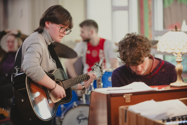 Photo of a person playing guitar beside a person playing the piano.