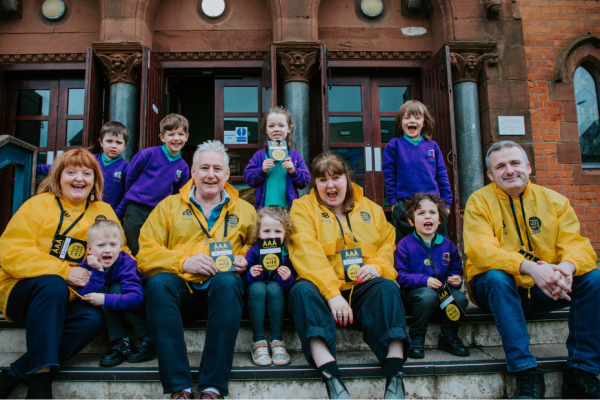a group of adults and children sitting on the steps of a building, looking at the camera and smiling