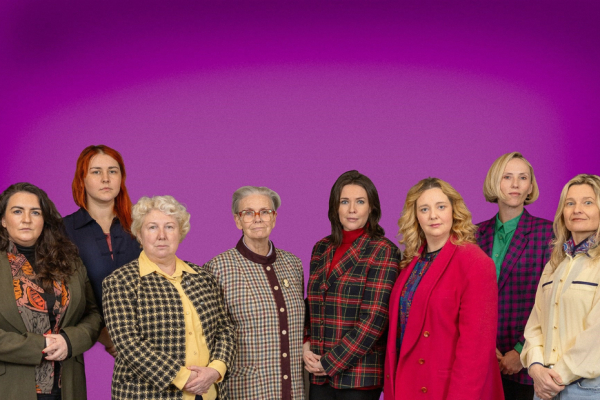 A group of women standing shoulder to shoulder in blazers and with serious expressions on their faces.