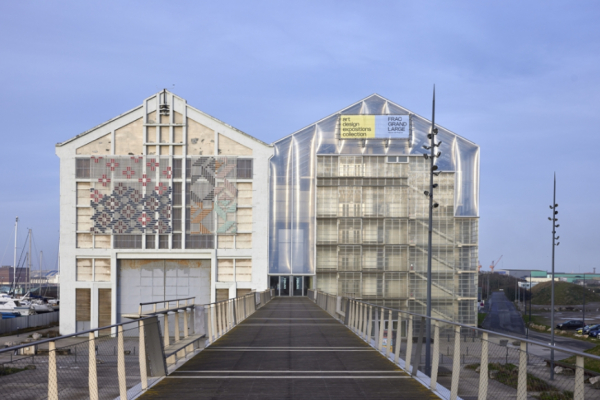 A grey building with a bridge in front of it