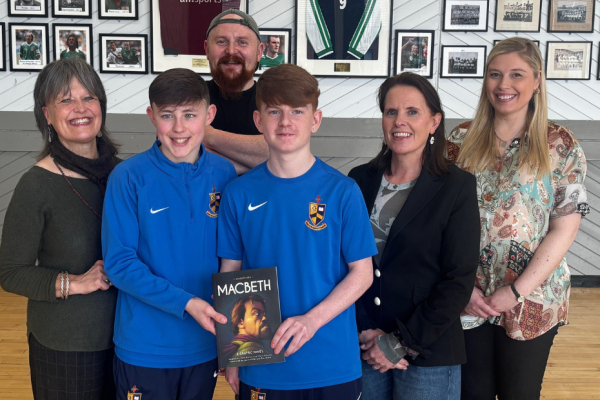 Two school pupils holding a macbeth book with four adults standing in a line