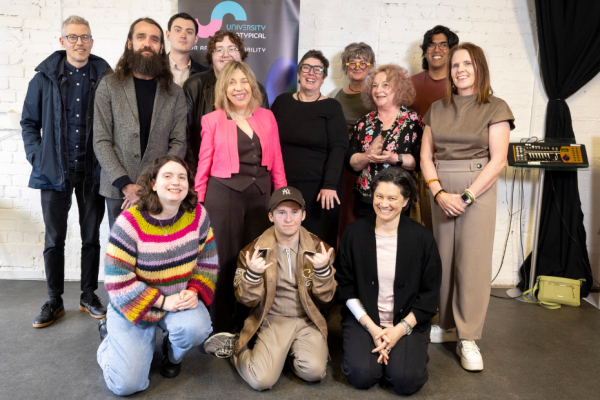 A group of men and women smiling for a group photo in front of a white wall