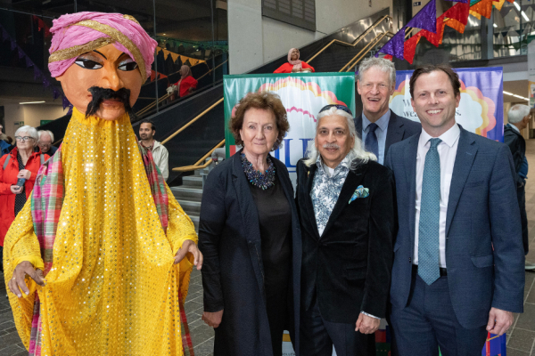A large Indian puppet in a yellow traditional costume, stands beside festival partners.