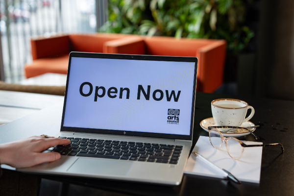 An open laptop with the words Open Now on the screen. A pair of glasses and a coffee cup are sitting beside it.