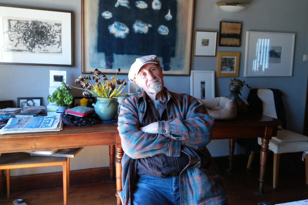 Male sitting folded arms in a studio wearing a flat cap and checked shirt.