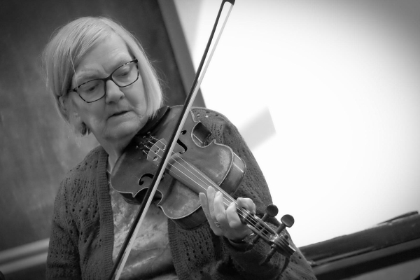 Lady with short hair and glasses playing the fiddle.