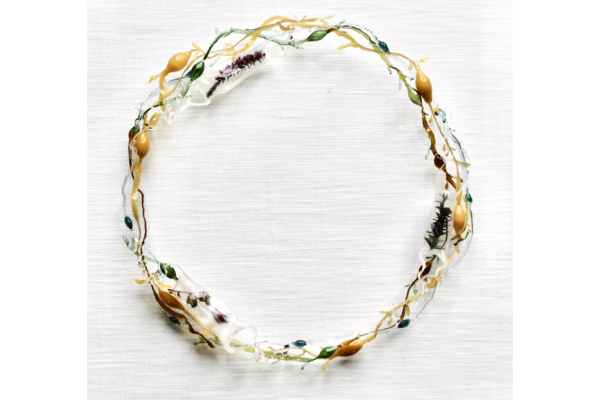 Circular glass wreath mounted onto a fabric background. Some of the hollow glass forms have organic matter and natural materials encapsulated within.