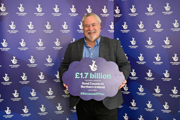 A man standing in front of a blue screen holding a sign about National Lottery funding