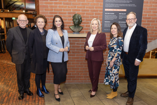 six people standing in a row in front of a statue, all looking at the camera and smiling.