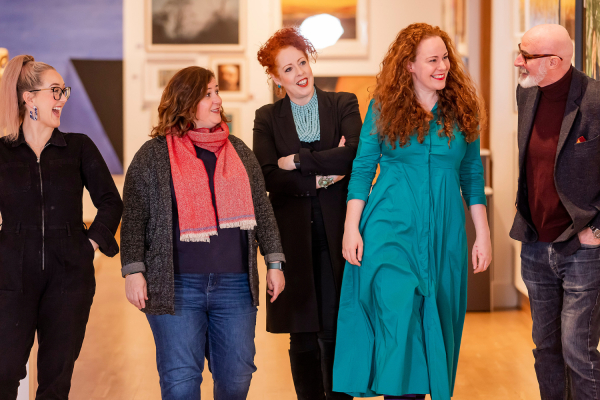 Five people walking through a gallery, seemingly sharing a joke