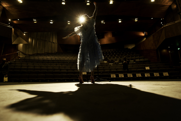 A silhouette figure is on stage, with an empty theatre in front of them
