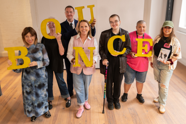 A group of people with disabilities holding individual yellow letters to spell out the word BOUNCE.