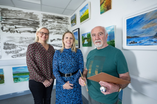 Three people standing in a gallery space with art on the walls.