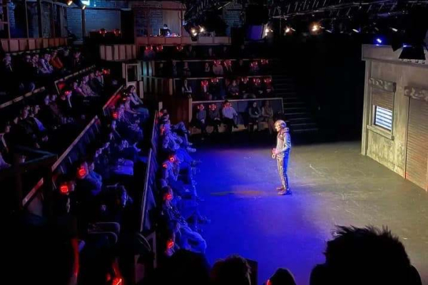 Man on a theatre stage, performing to a crowd.