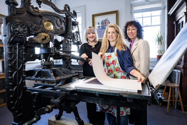 Image of three people in front of a large printing press