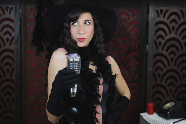Female singer wearing a black dress, black hat and a black feather boa.