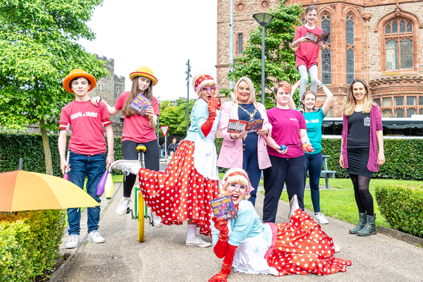 Group of street performers outside the Guildhall in Derry-Londonderry with three females holding the programme for the 2022 Carnival of Colours.