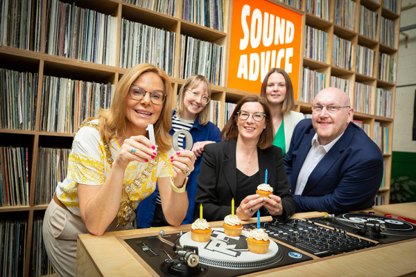 Four females and one male stood beside Dj Decks holding cupcakes with candles and a wall of music records in the background.
