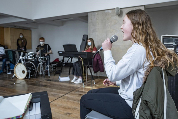 Young Jazz singer performing holding microphone with a jazz drummer and pianist in the background.