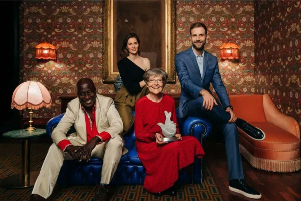 An image of four people sitting on a sofa in a room with colourful wallpaper. One person is holding a national lottery trophy.
