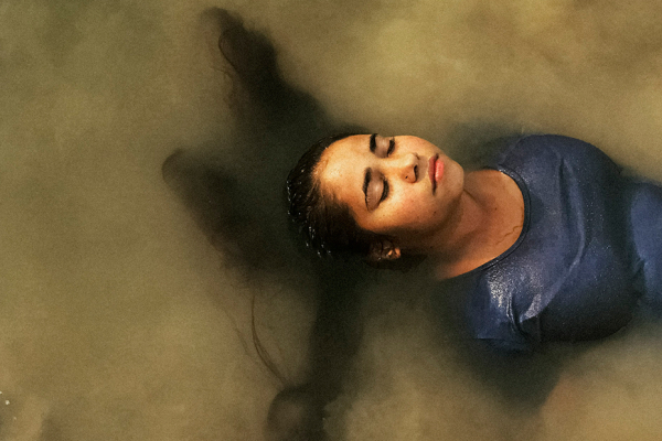 Female with long dark hair and a blue top partially submerged in cloudy water.