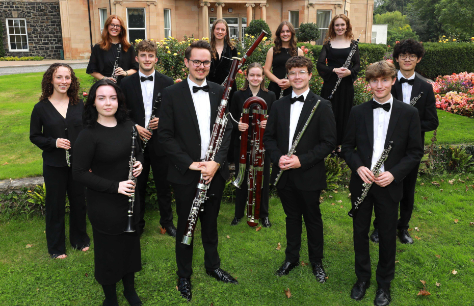 A group of woodwind musicians in black tie formal wear pose as a group with their instruments.