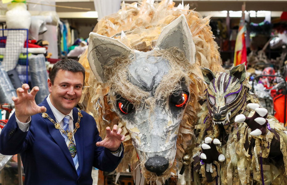 A man in a blue suit pictured with a large, papier-mâché model of a wolf.