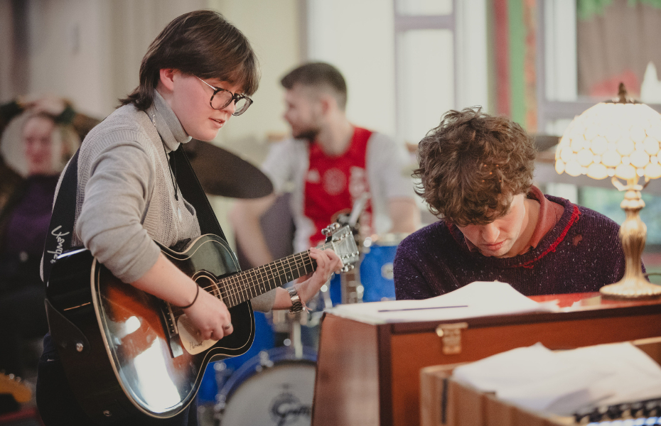 Photo of a person playing guitar beside a person playing the piano.