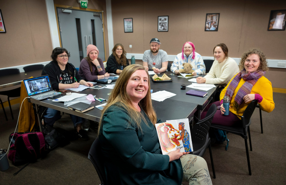 A group of people sitting around a large desk with pens and paper in front of them.