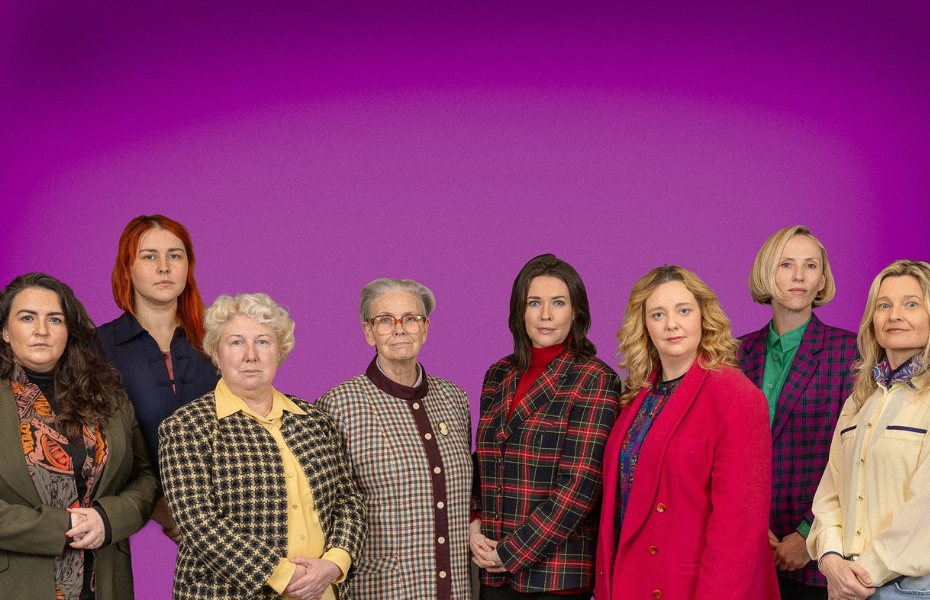 A group of women standing shoulder to shoulder in blazers and with serious expressions on their faces.