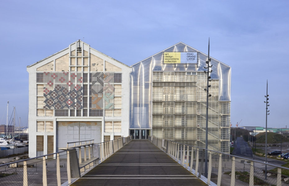 A grey building with a bridge in front of it