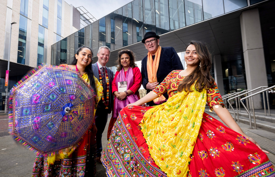 People standing outside Ulster University.  Indian dancers are wearing bright, colourful traditional costumes and holding a decorated colourful Indian umbrella.