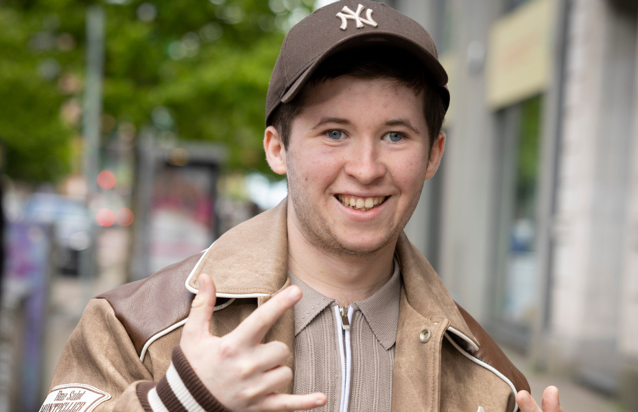 a young man smiling at the camera wearing a baseball cap and holding his hands up