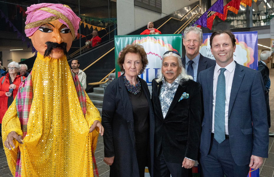 A large Indian puppet in a yellow traditional costume, stands beside festival partners.