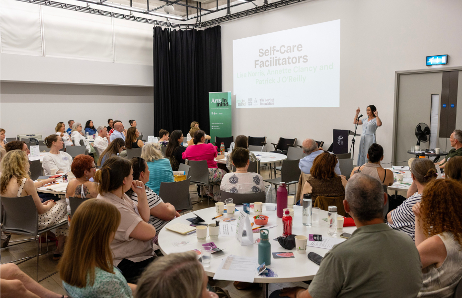 Event space with people sitting around round tables looking at a stage with a woman talking at a podium