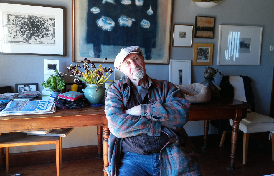 Male sitting folded arms in a studio wearing a flat cap and checked shirt.