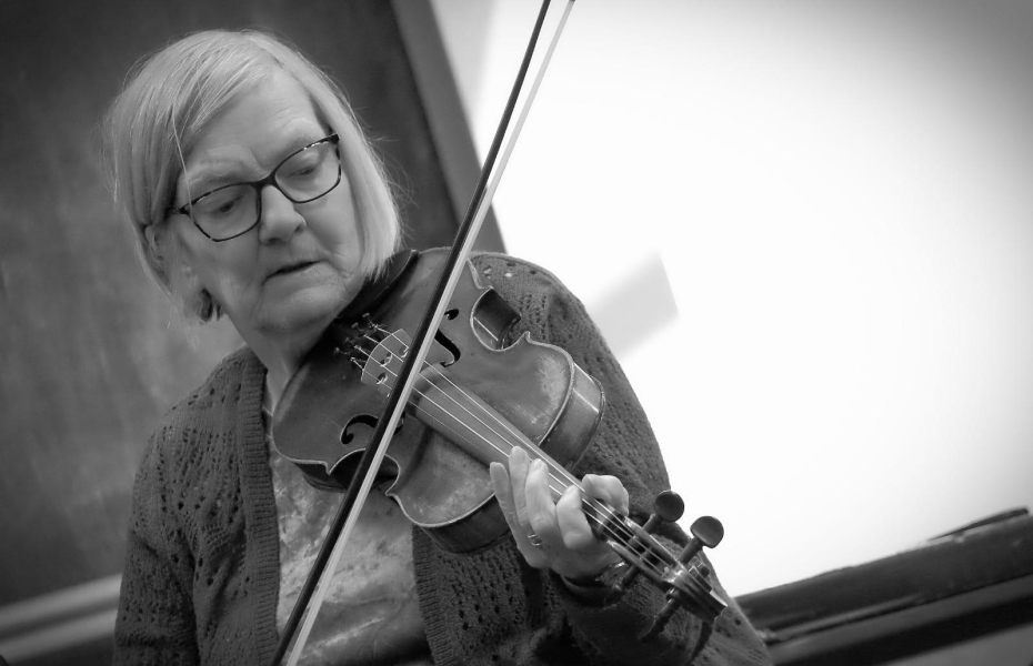 Lady with short hair and glasses playing the fiddle.