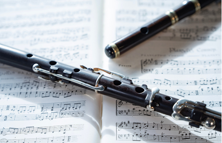 white sheet of music with a black flute lying on top of it