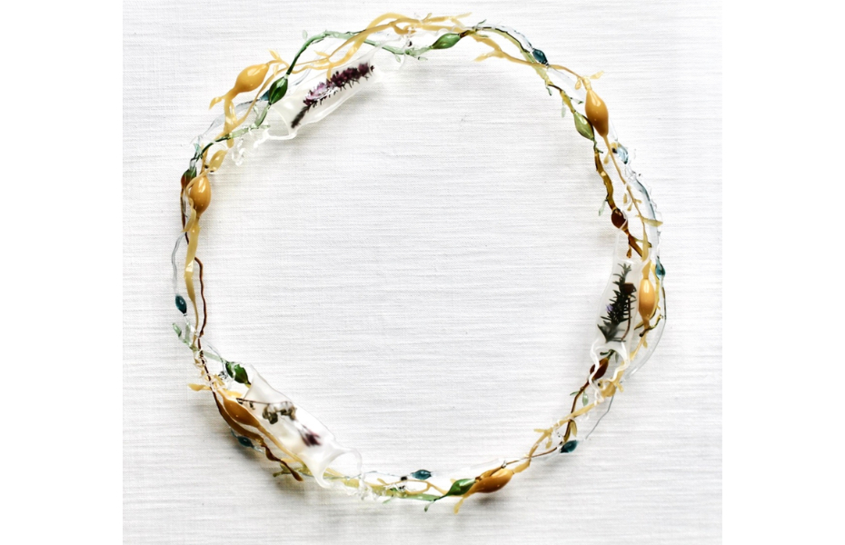 Circular glass wreath mounted onto a fabric background. Some of the hollow glass forms have organic matter and natural materials encapsulated within.