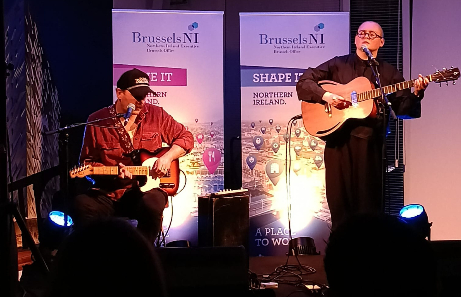 A man playing a guitar and a woman playing guitar and singing on a stage