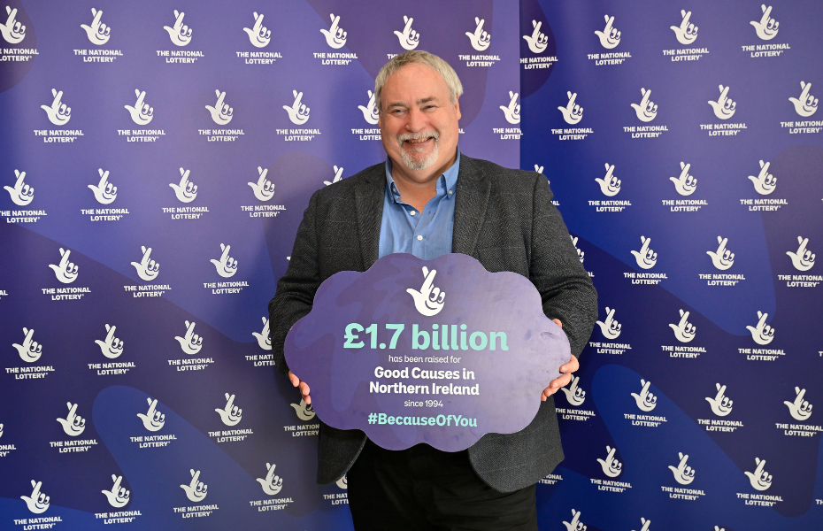 A man standing in front of a blue screen holding a sign about National Lottery funding