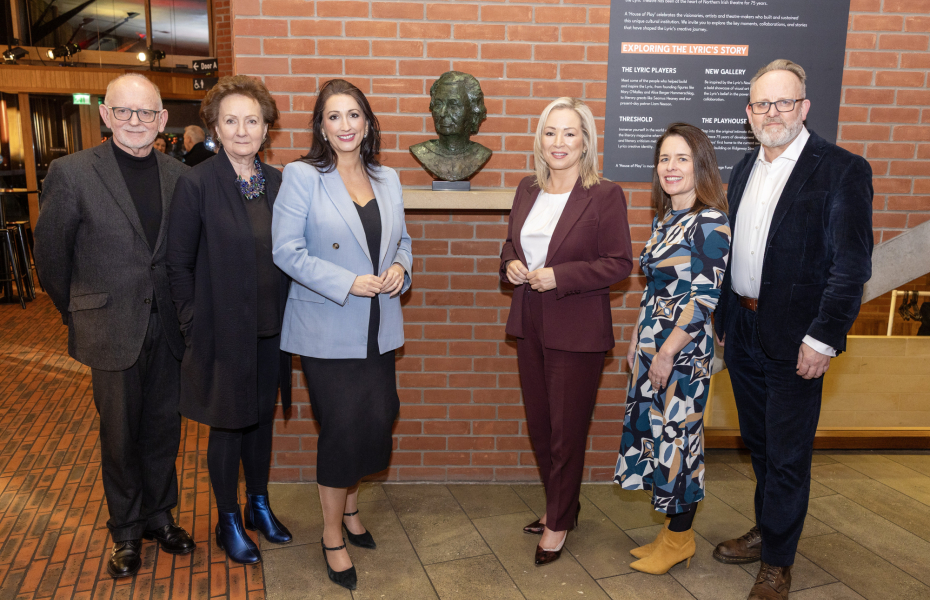 six people standing in a row in front of a statue, all looking at the camera and smiling.